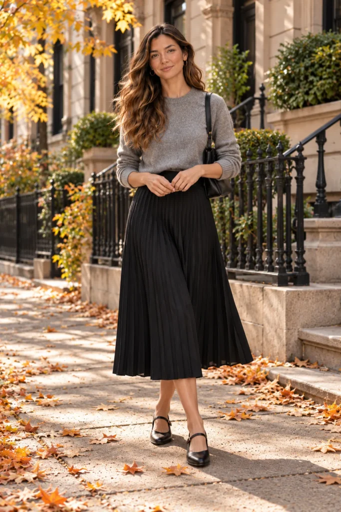 Grey cashmere sweater tucked into black pleated midi skirt with Mary Jane flats
